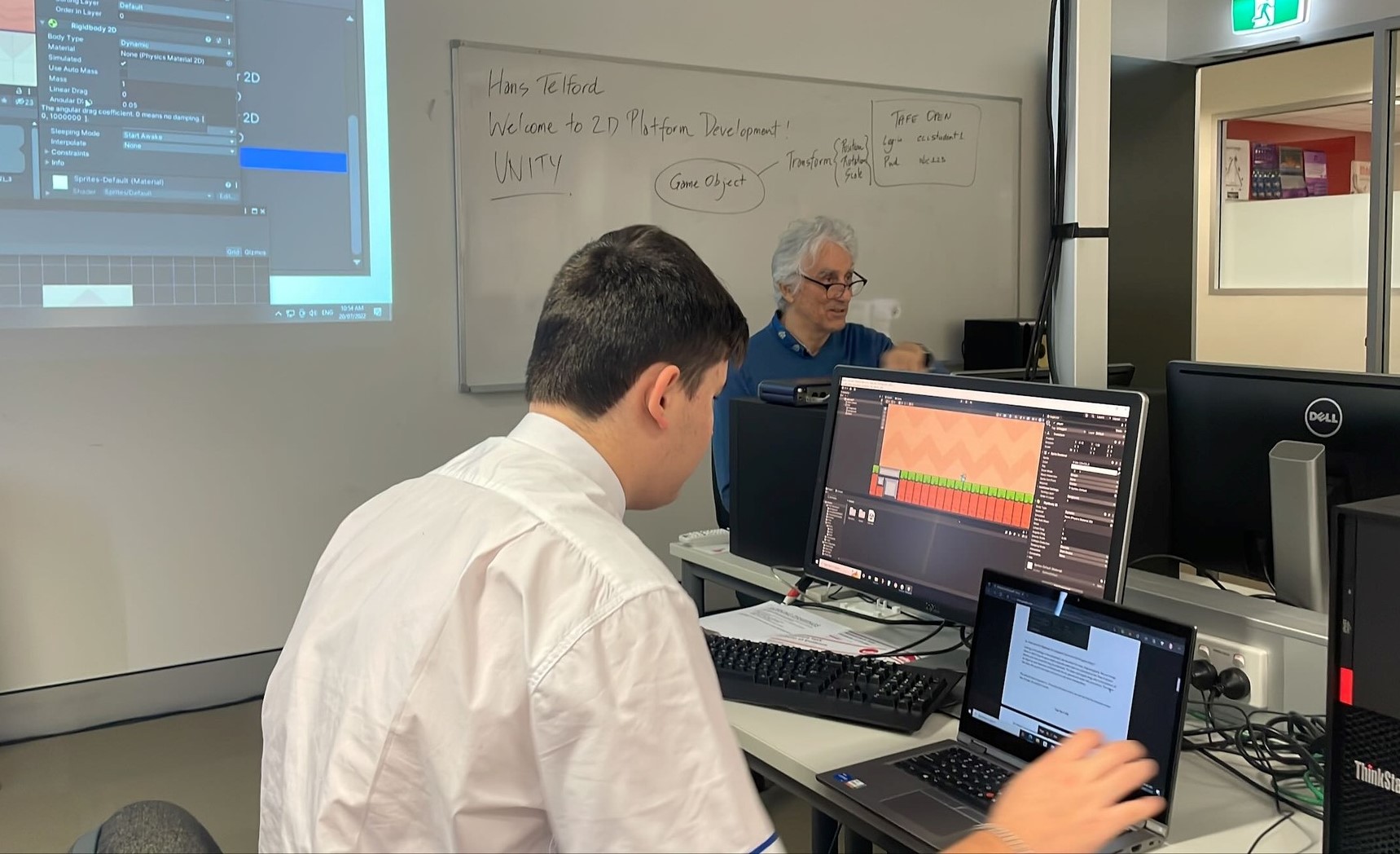 Student developing a digital project using computer software with teacher guidance highlighting programming skills and applied digital learning