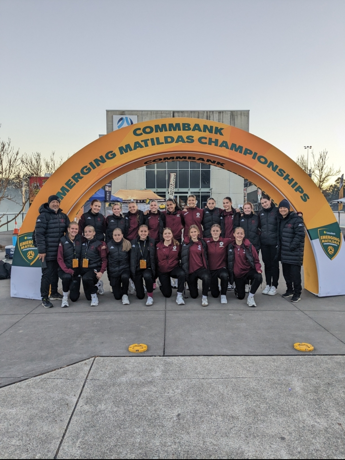 College team group photo under Emerging Matildas Championships signage highlighting teamwork pride and representation at a major sporting competition