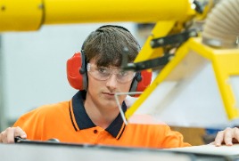 Student using industrial machine with safety equipment in workshop environment