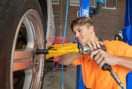Student working on a car wheel using pneumatic tools in automotive workshop